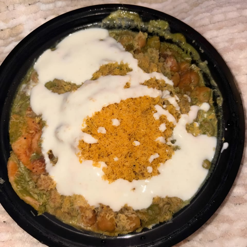 Top-down view of an Indian dish with green curry, chickpeas, white sauce, and orange crispy topping.