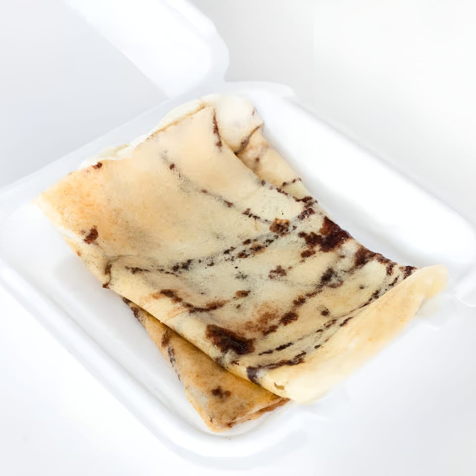 Two folded Indian crepes, light brown with dark brown speckles, rest in a white container.