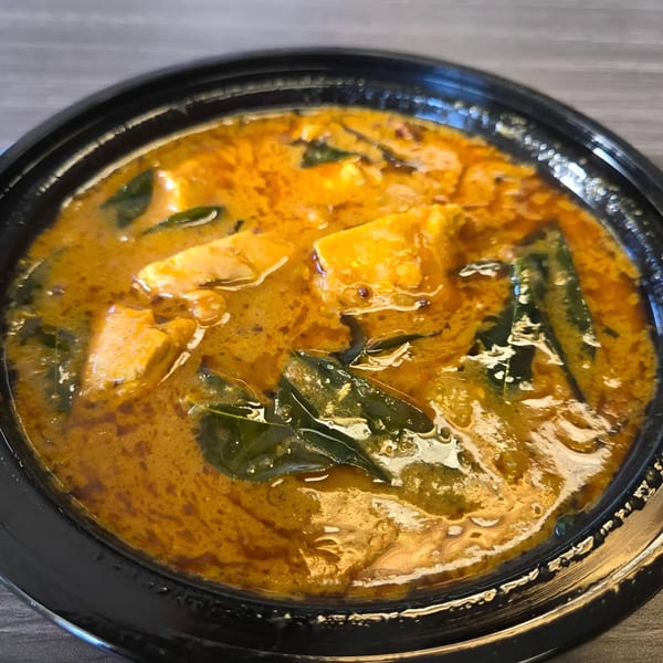Close-up of a vibrant orange Indian curry with paneer and green leaves in a black bowl.