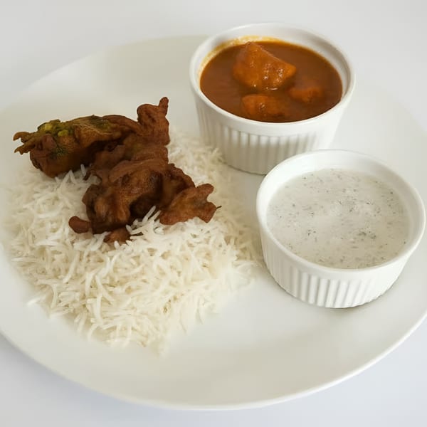 Indian meal with rice, pakora, chicken curry, and raita on a white plate.